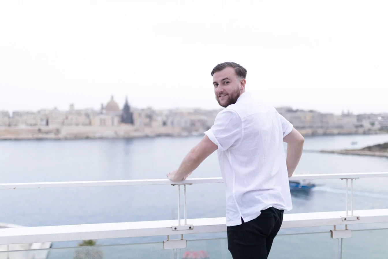 Théo Bayoux accoudé à une rambarde, se retournant vers l'objectif, la mer derrière lui