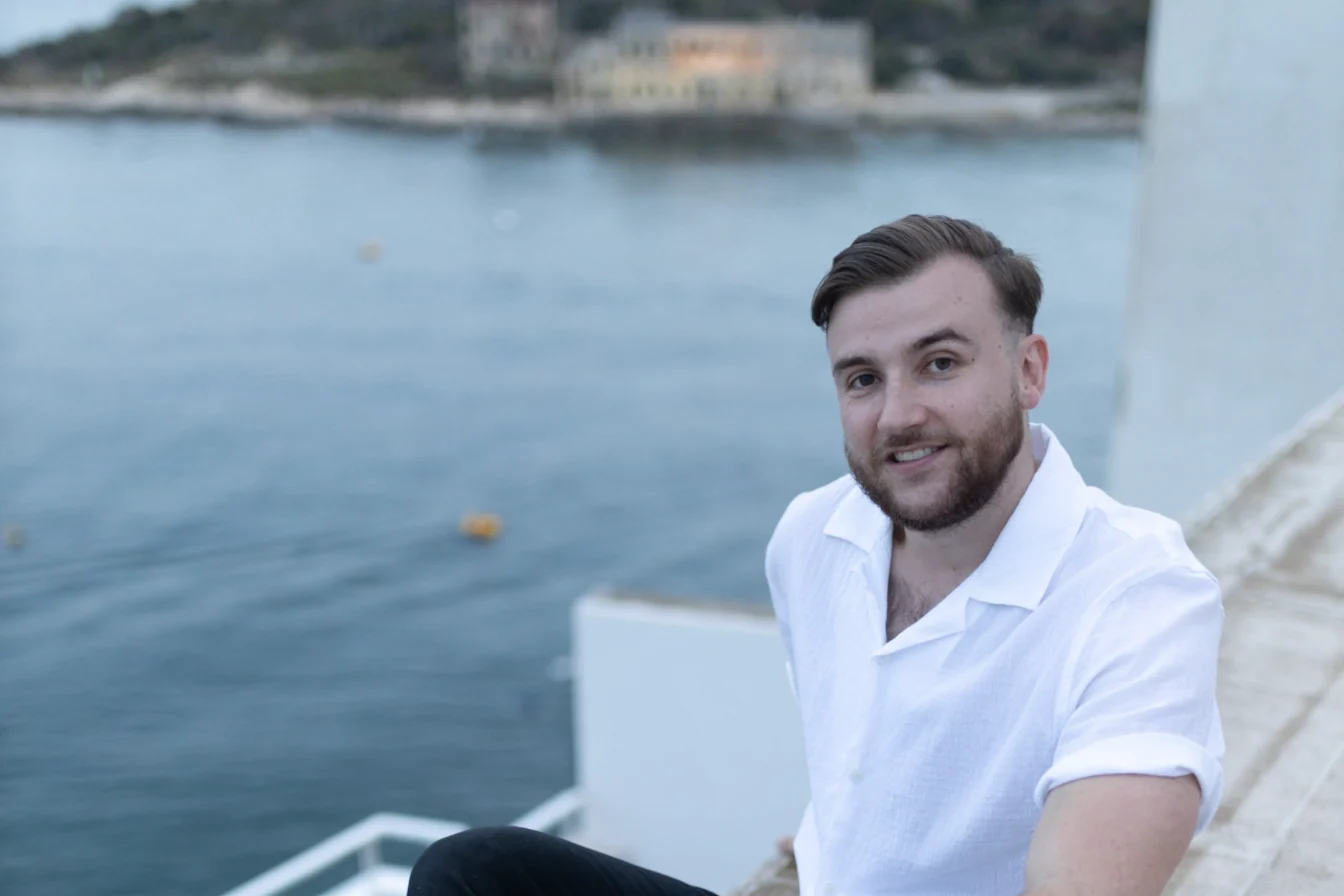 Théo Bayoux assis sur la terrasse, la mer derrière lui