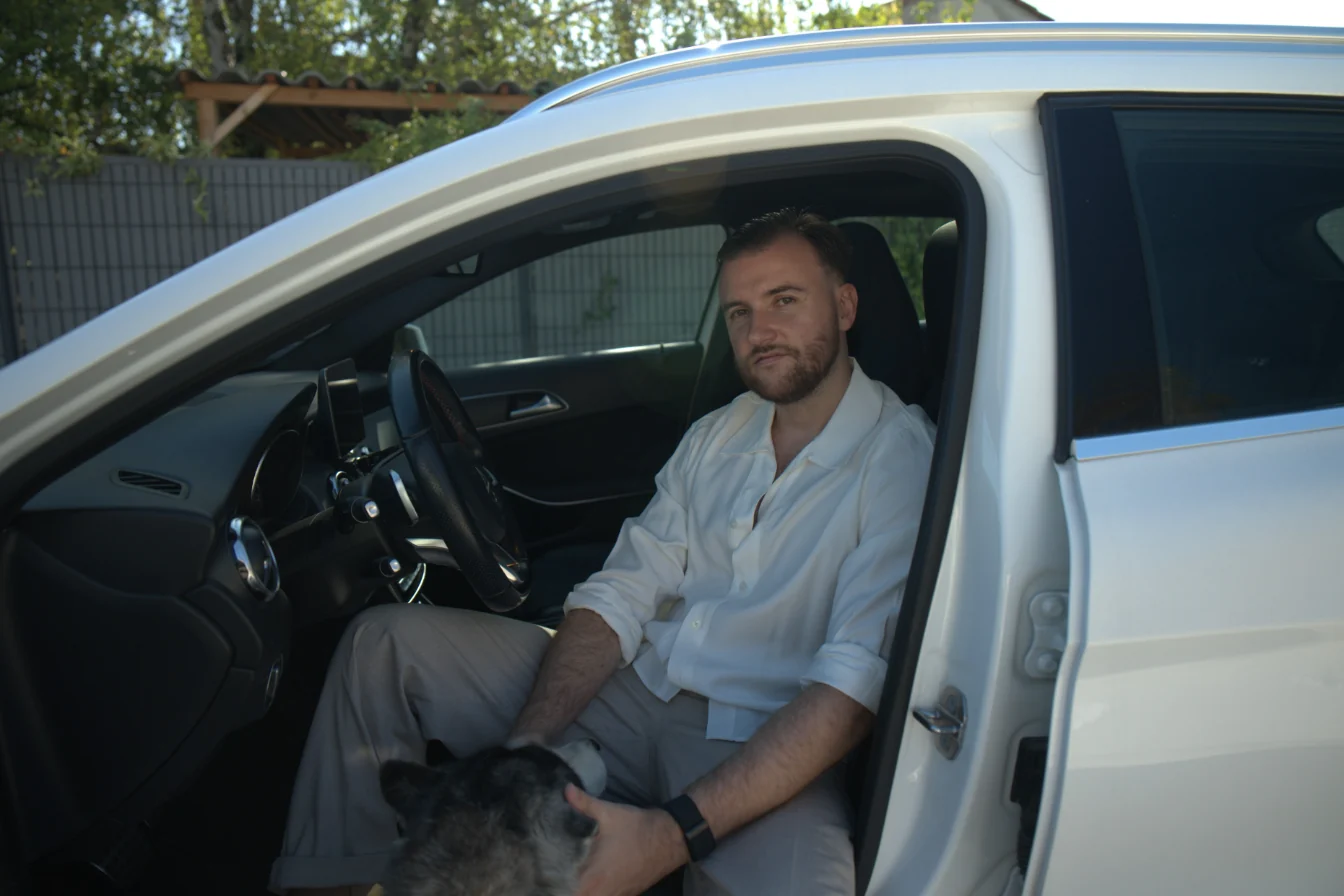 Théo Bayoux assis dans sa voiture, portière ouverte, avec son husky